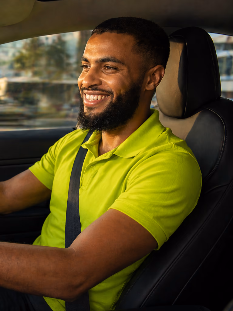 A smiling GuyWay driver in a branded yellow polo at the wheel of an electric Tesla in Georgetown — vetted drivers, traceable trips, real safety team on call