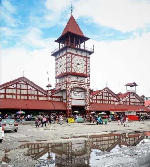 Stabroek Market clock tower rising above the red-and-white roofs of central Georgetown, crowds and vendors below.