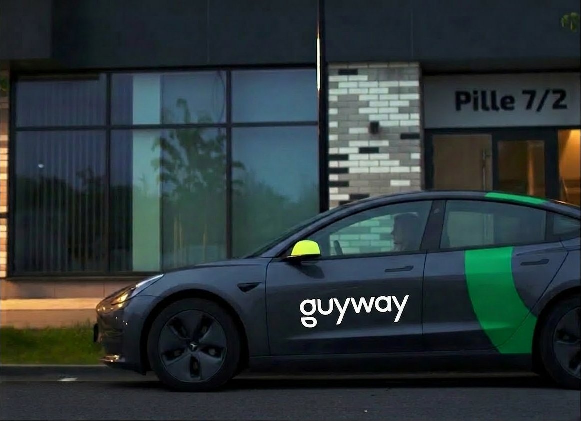 A branded GuyWay Tesla parked outside a modern Georgetown building at dusk — the electric vehicle you'll drive on the GuyWay platform