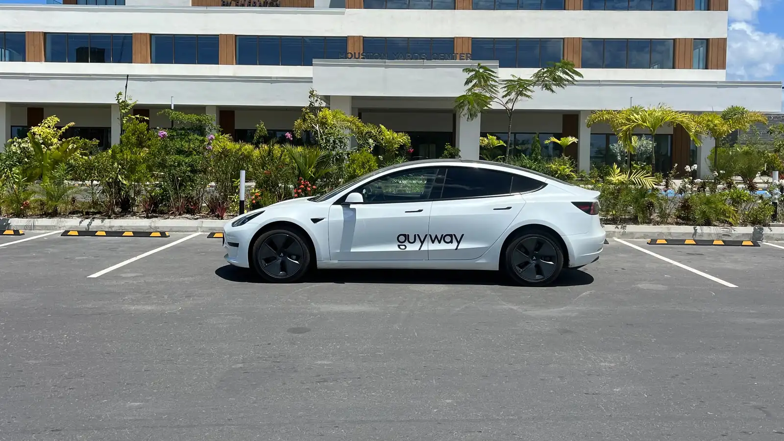 Witte GuyWay-Tesla Model 3 geparkeerd voor het gebouw van Houston Yards Center