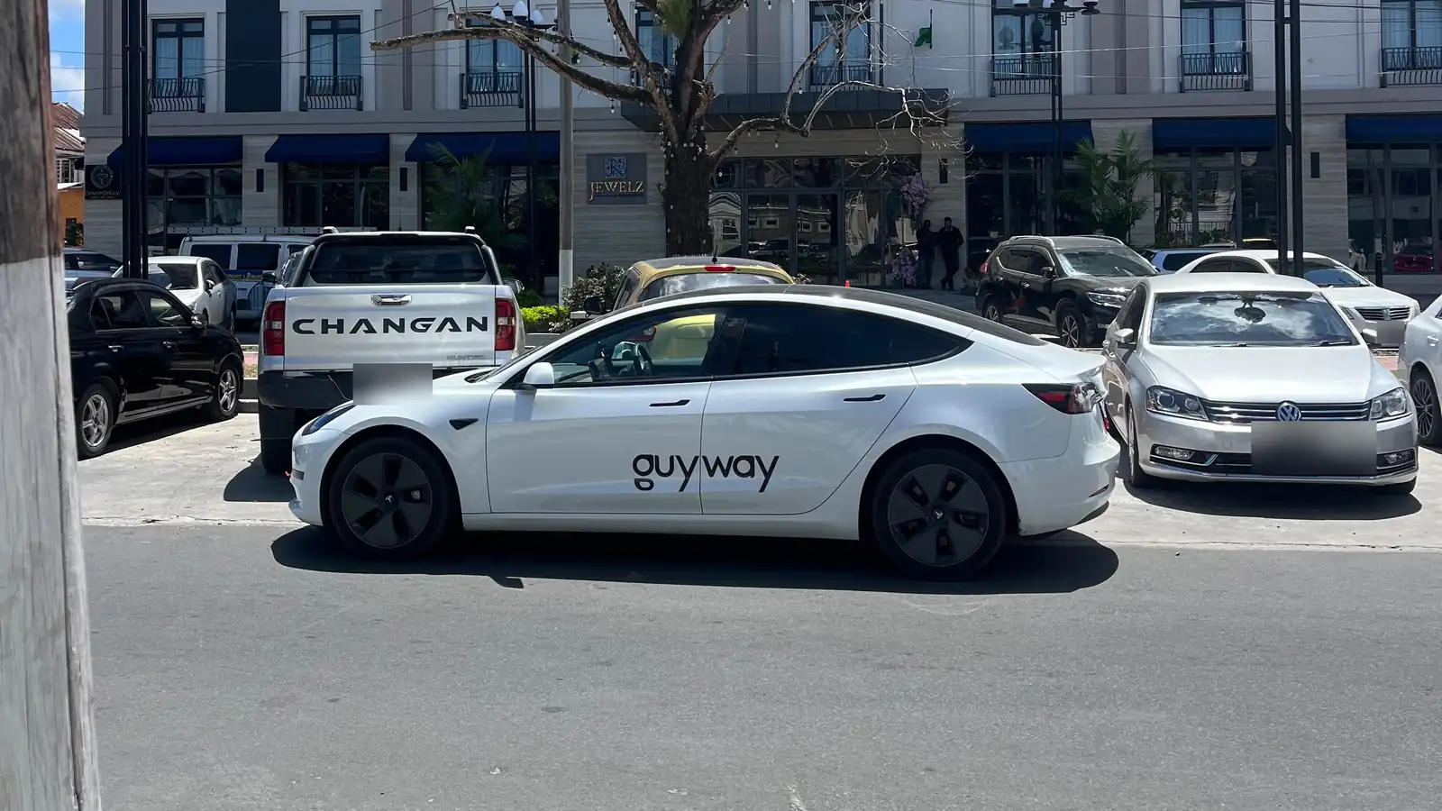 Tesla Model 3 blanco de GuyWay estacionado en la calle frente al King's Hotel, Georgetown