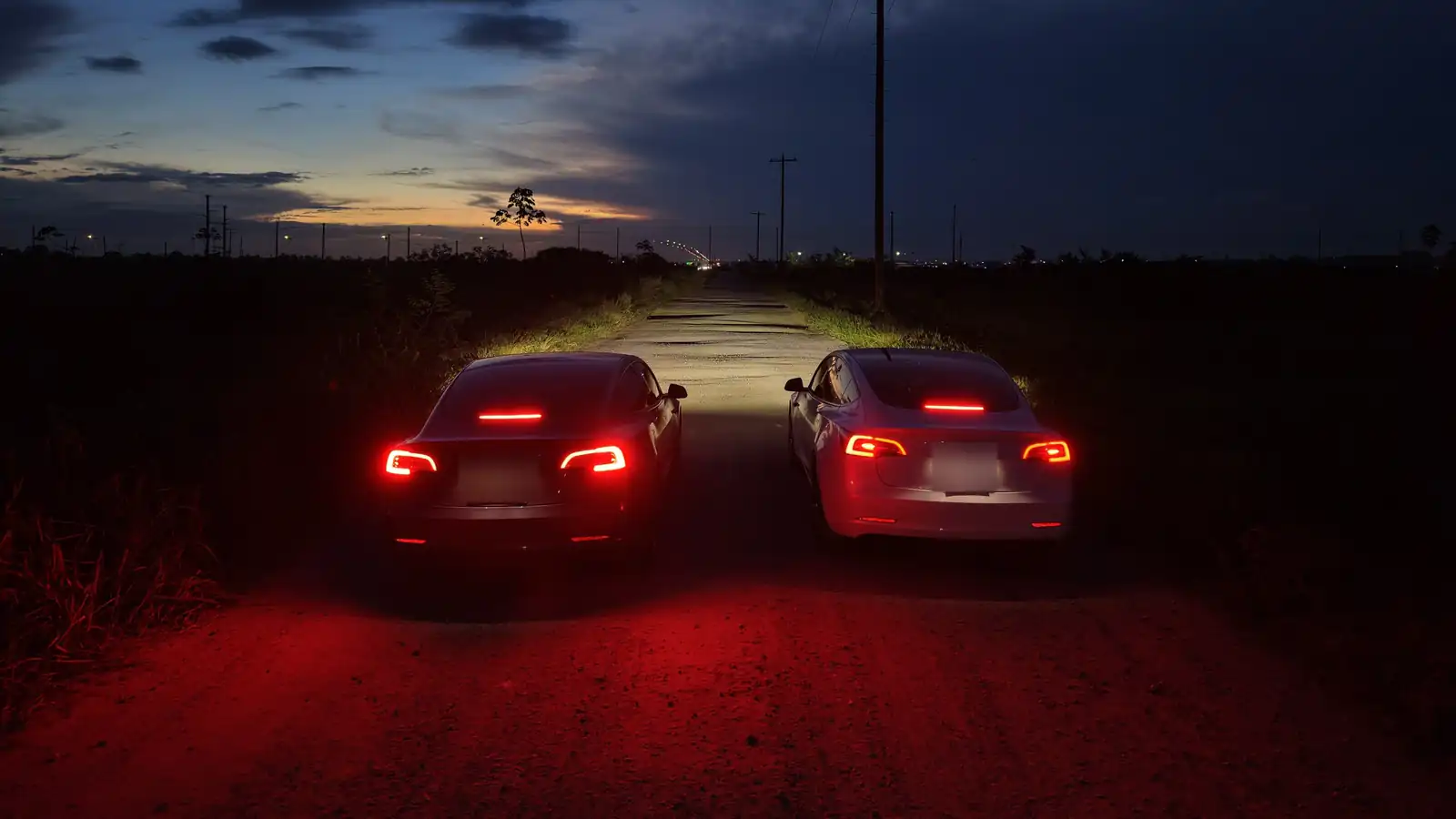 Twee Tesla’s met brandende achterlichten op een onverlichte weg in de schemering