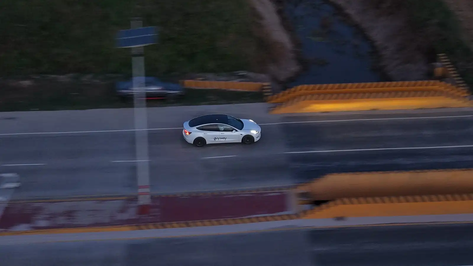 White GuyWay Tesla Model 3 driving on a highway at dusk, seen from above