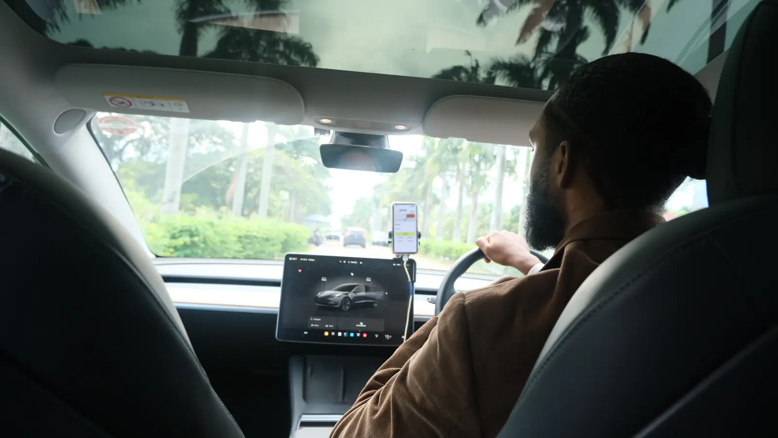 Inside a GuyWay Tesla: the driver at the wheel seen from behind, the centre touchscreen and a phone mount