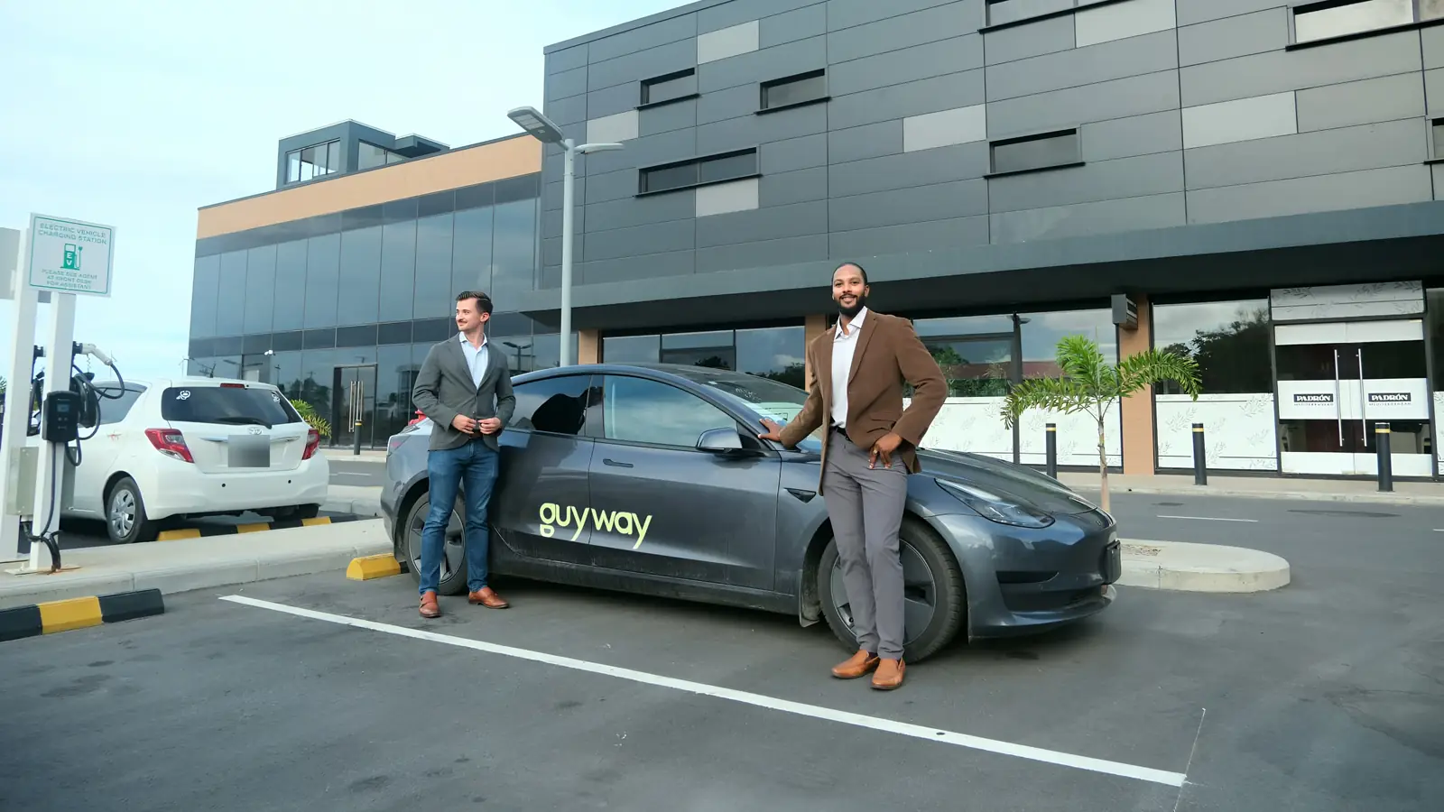 Dos integrantes del equipo de GuyWay junto a un Tesla de GuyWay en el estacionamiento de un hotel