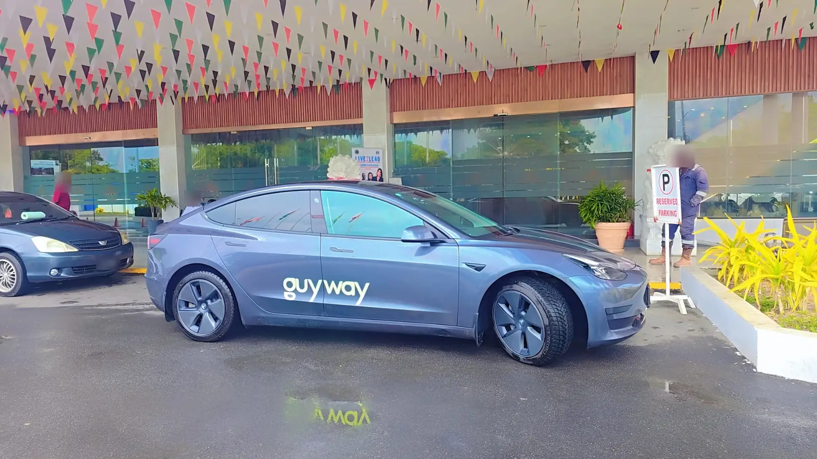Tesla Model 3 de GuyWay en la entrada de un hotel bajo banderines festivos