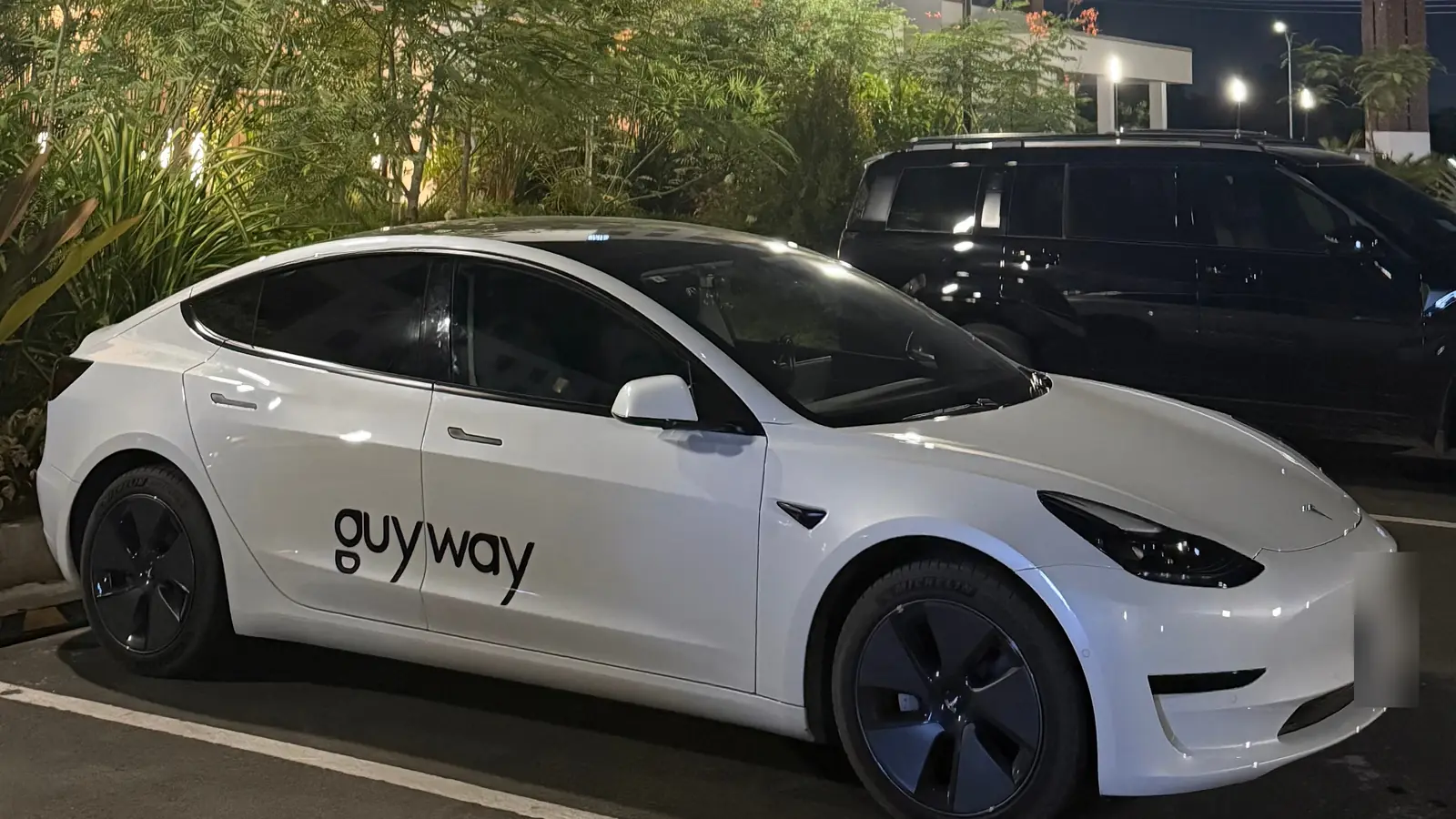 White GuyWay Tesla Model 3 parked at night, ready for a booked ride
