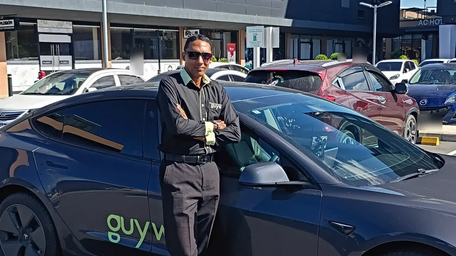 A GuyWay driver in uniform standing in front of a GuyWay Tesla