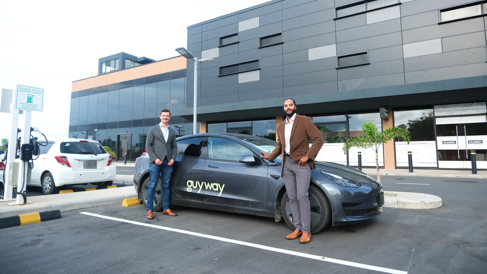 Two GuyWay team members in blazers beside a GuyWay Tesla outside a hotel in Georgetown