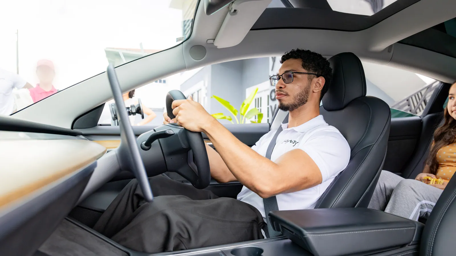 A GuyWay driver in a GuyWay polo at the wheel of a Tesla, a rider in the back seat