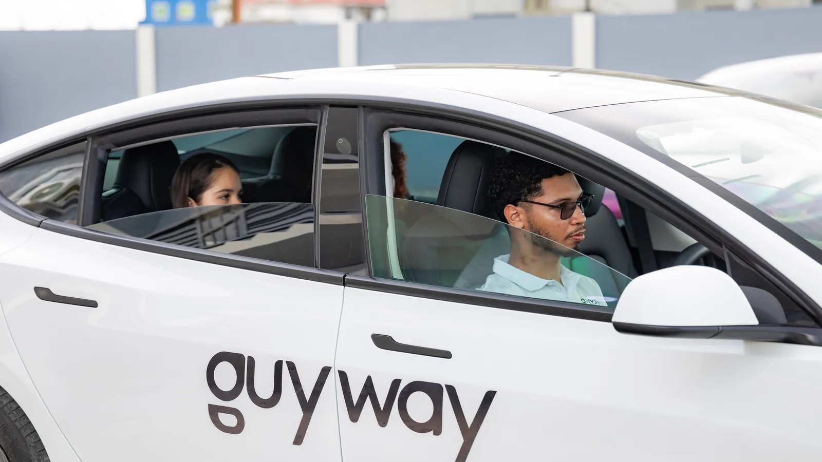 A GuyWay driver seen through the window of a white GuyWay Tesla