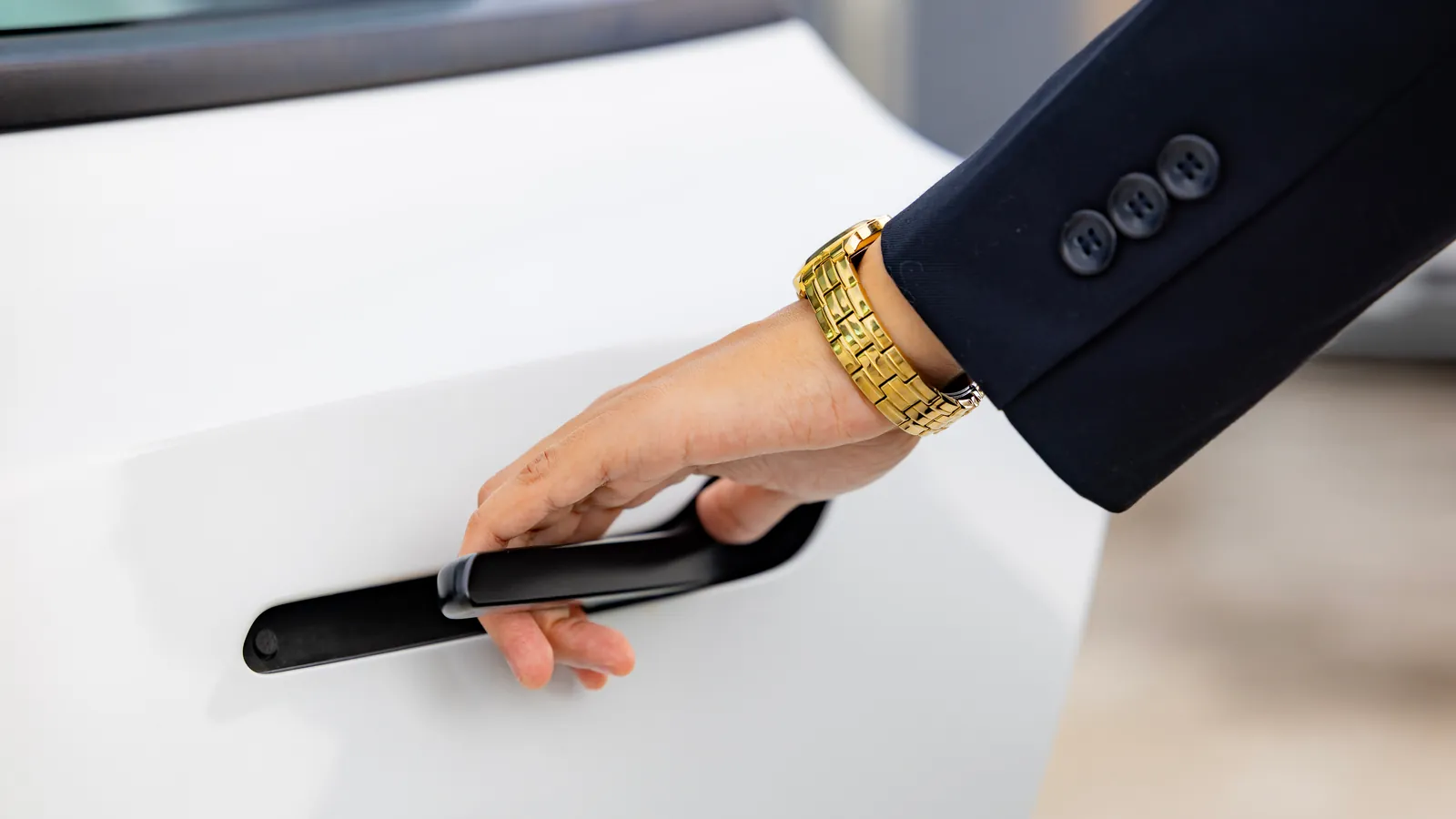A rider in a navy suit opens the flush door handle of a white GuyWay Tesla