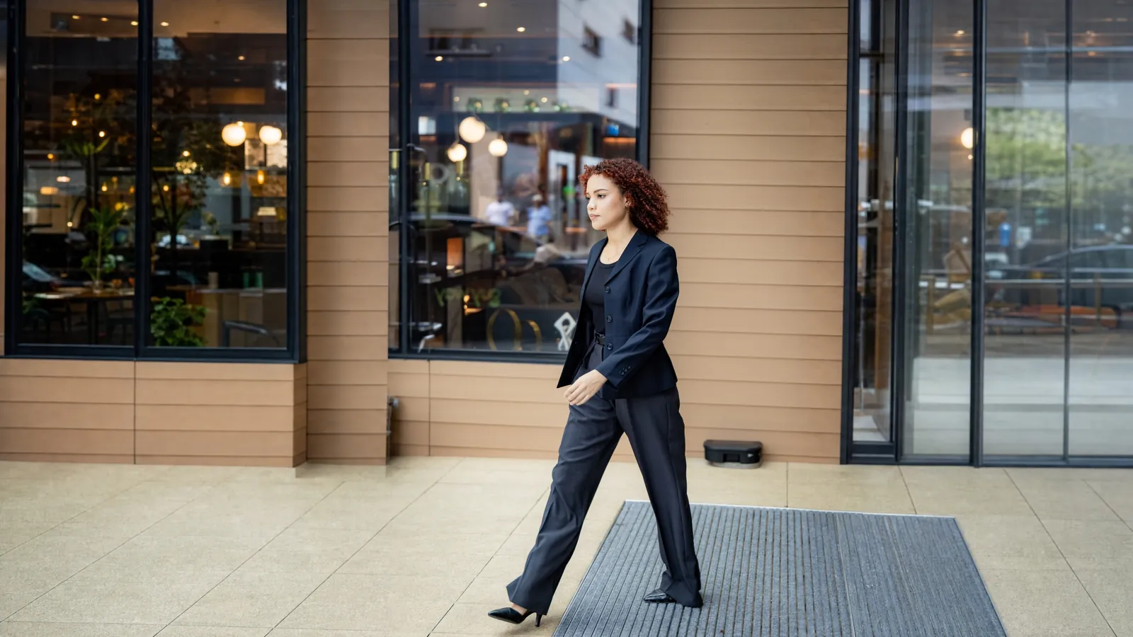 A GuyWay rider in a navy suit walks past glass shopfronts