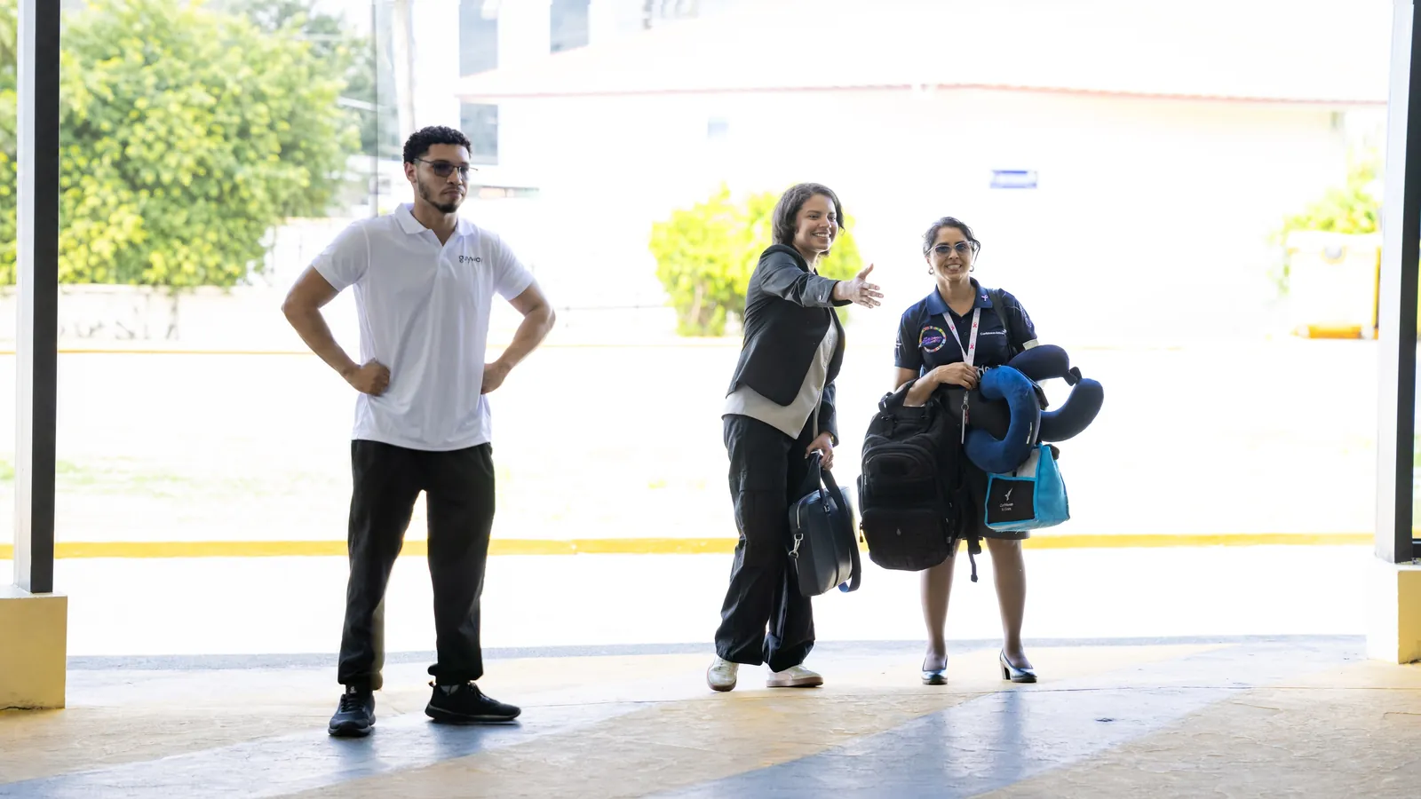 A GuyWay team member welcomes two travellers with their bags outside the terminal at Cheddi Jagan International Airport