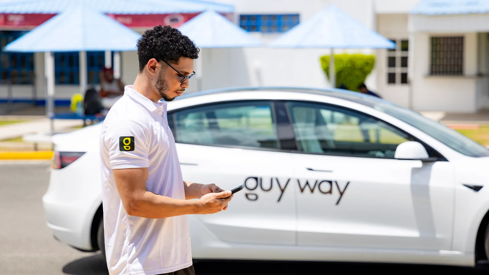 A GuyWay team member checks his phone beside a white GuyWay Tesla