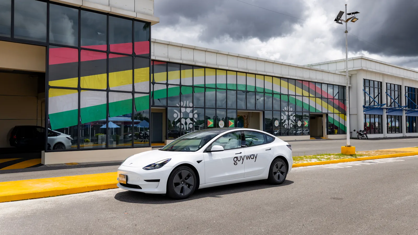 White GuyWay Tesla Model 3 at the CJIA terminal, its windows painted in the colours of the Guyana flag