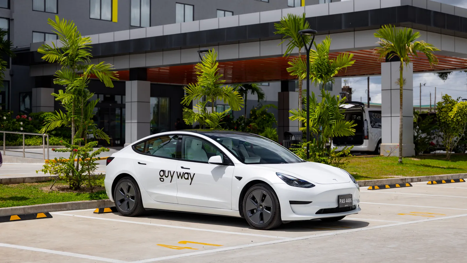 White GuyWay Tesla Model 3 in front of the entrance of the Courtyard by Marriott near Cheddi Jagan International Airport