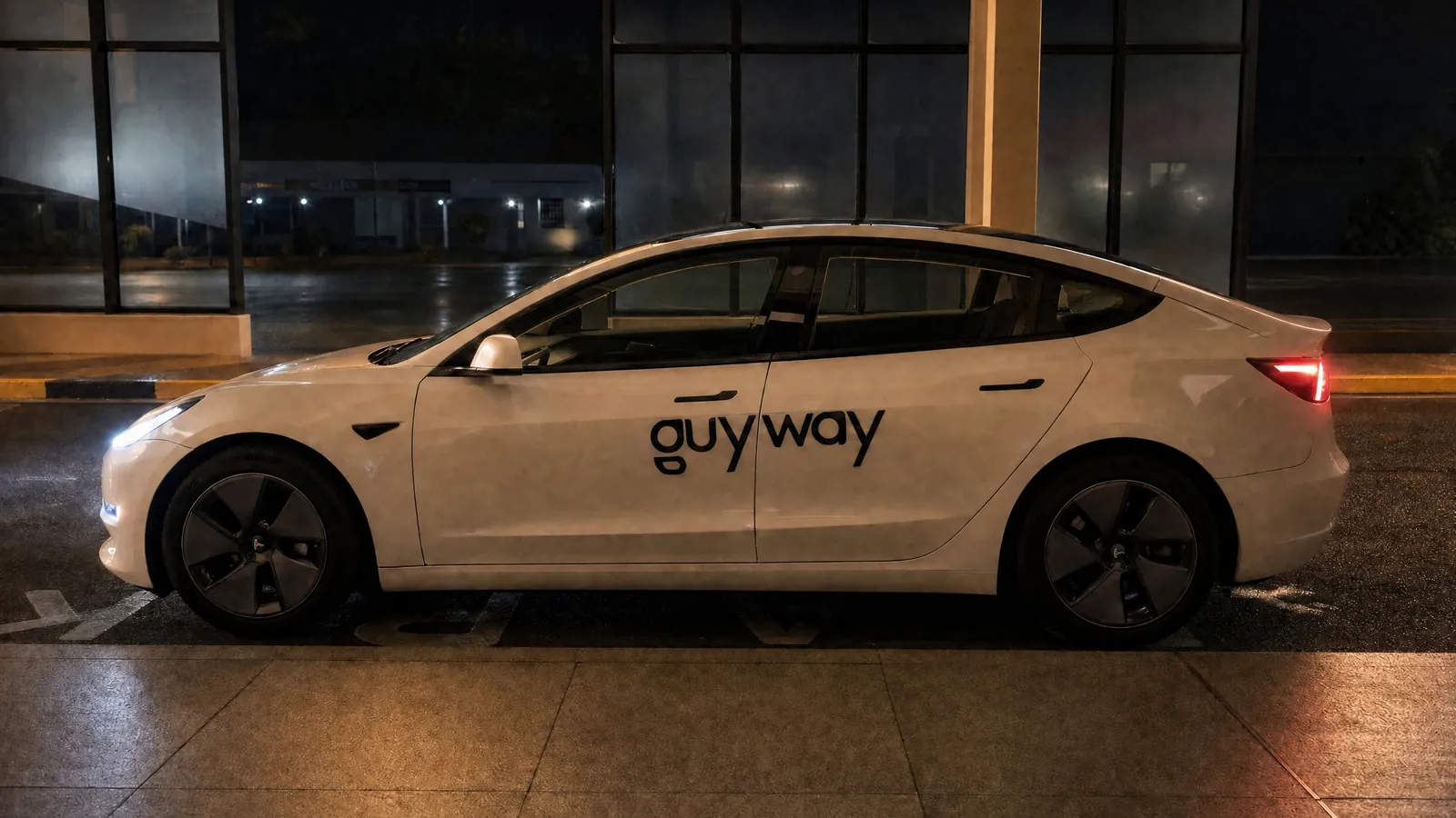 White GuyWay Tesla Model 3 with its lights on at the departures kerb of Cheddi Jagan International Airport before dawn