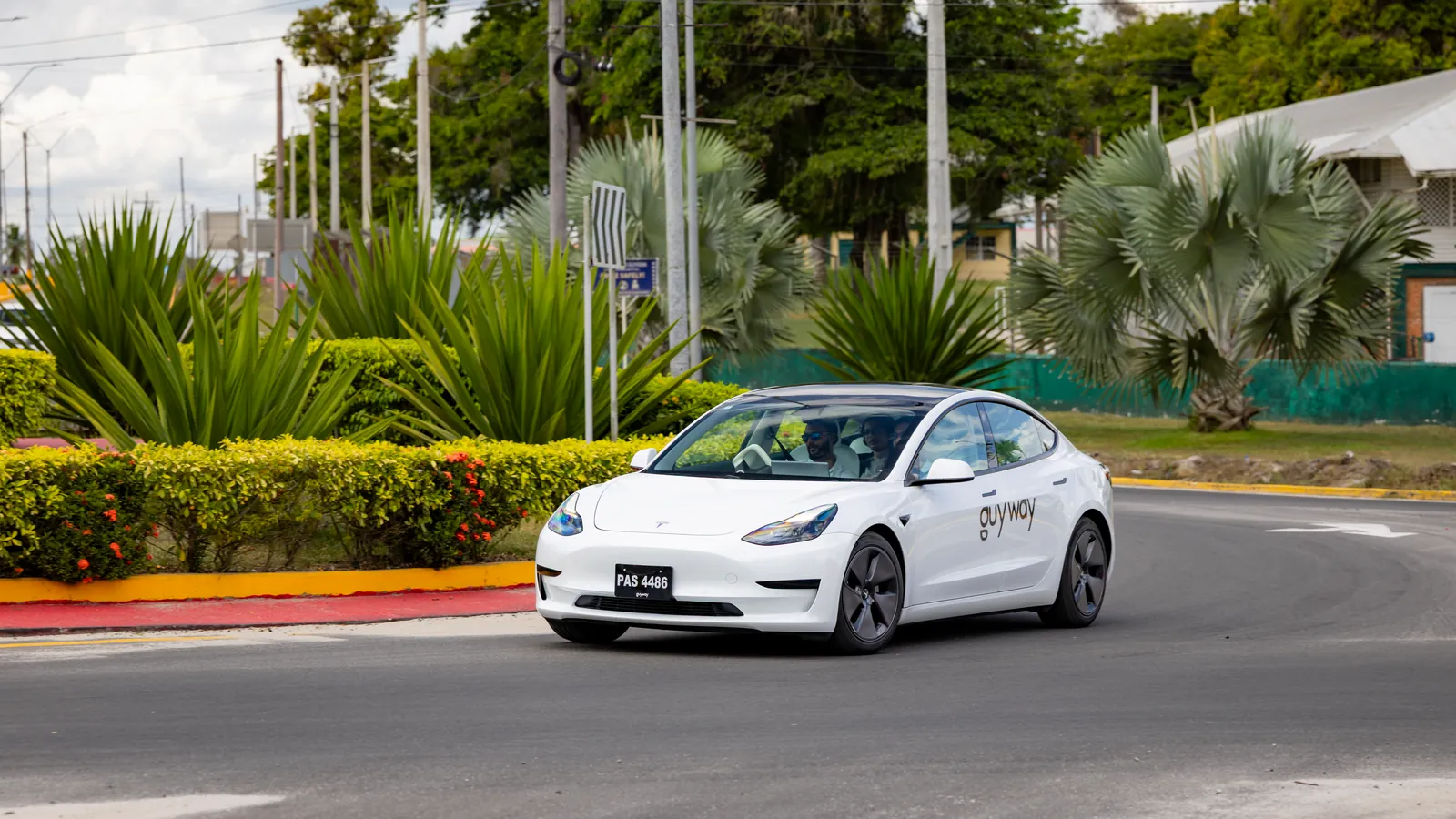 White GuyWay Tesla Model 3 on a tree-lined roundabout on the East Bank