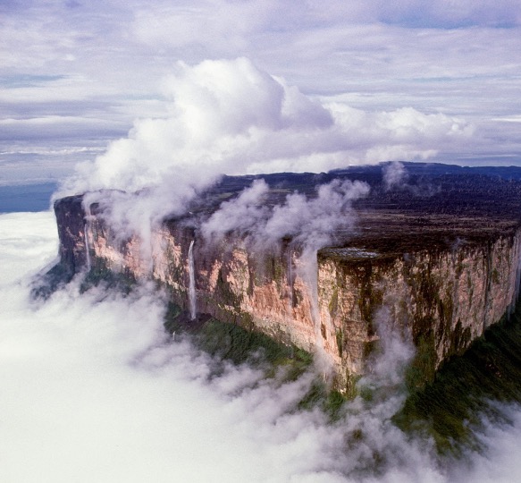 Mount Roraima tepui rising through clouds, waterfalls cascading down its sheer cliff walls.
